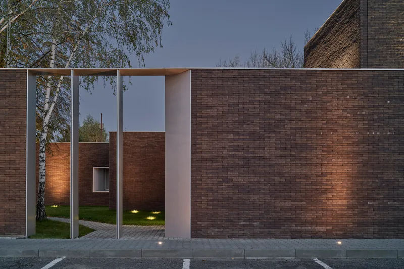 Dark brick wall with a framed entry portal and recessed lighting at twilight