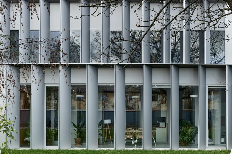 Close-up of the white vertical fin facade with alternating glazed openings reflecting bare branches