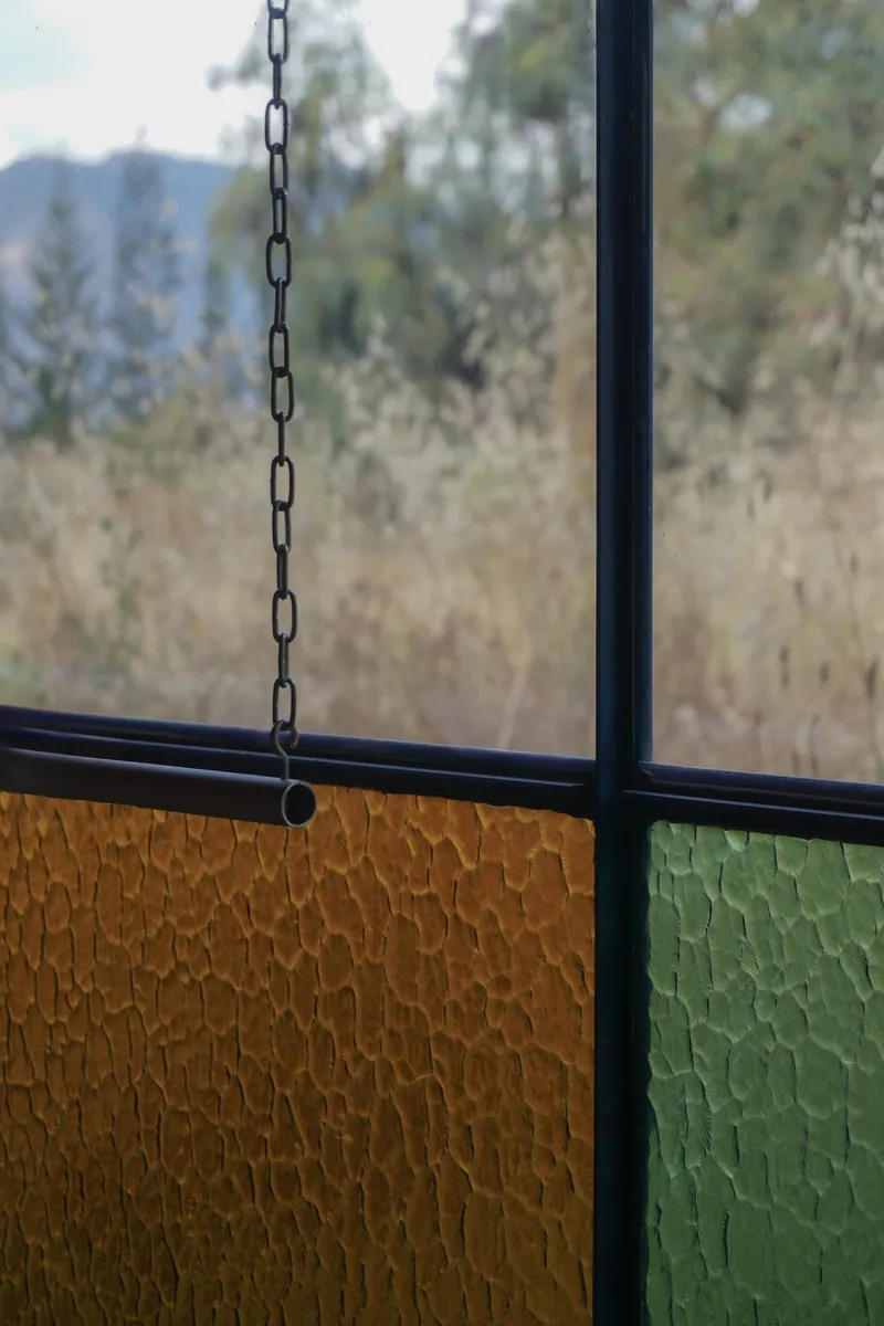 Close-up of textured yellow and green glass panels with a suspended metal chain in the foreground