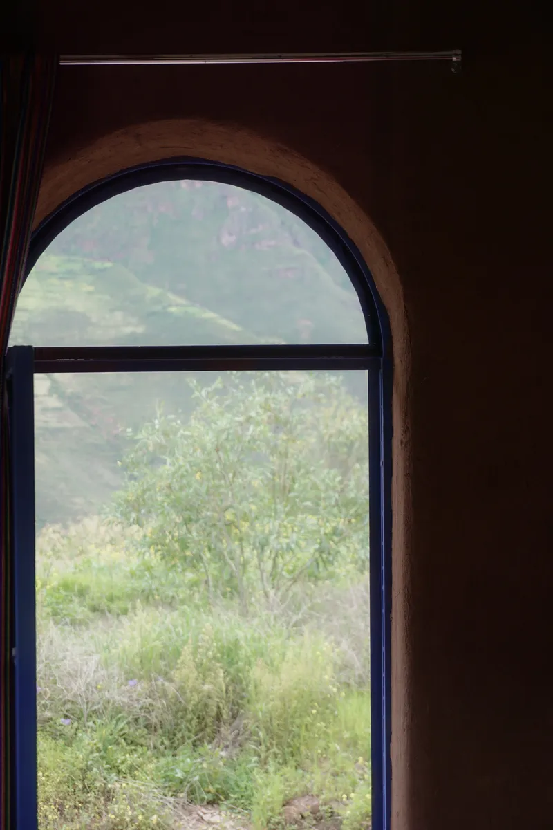 Arched window opening framing green foliage and hillside through dark earthen walls