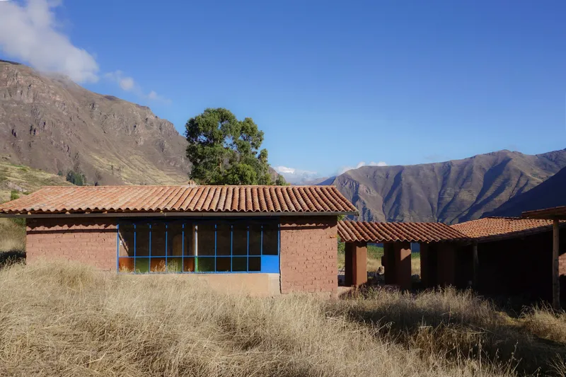 Adobe brick structures with clay tile roofs set in dry grassland below a ridged mountain