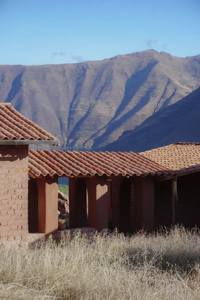 Clay tile roofs and adobe walls with shadows cast by afternoon sun and mountains beyond