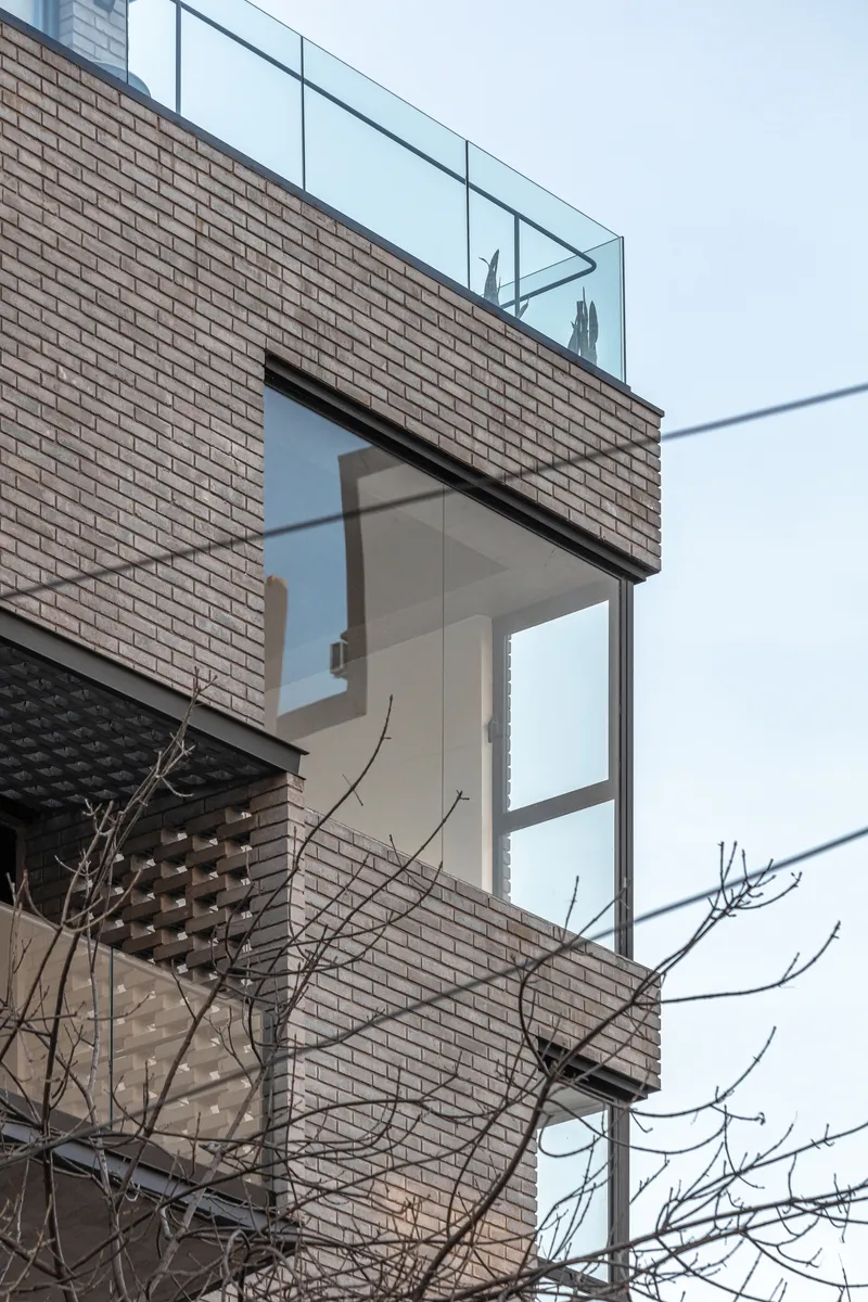 Detail of stacked balconies with perforated brick screens and bare tree branches in the foreground