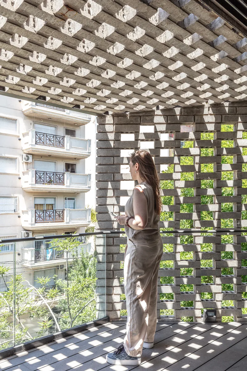 Balcony view through the perforated brick screen creating dappled shadows with a person standing inside