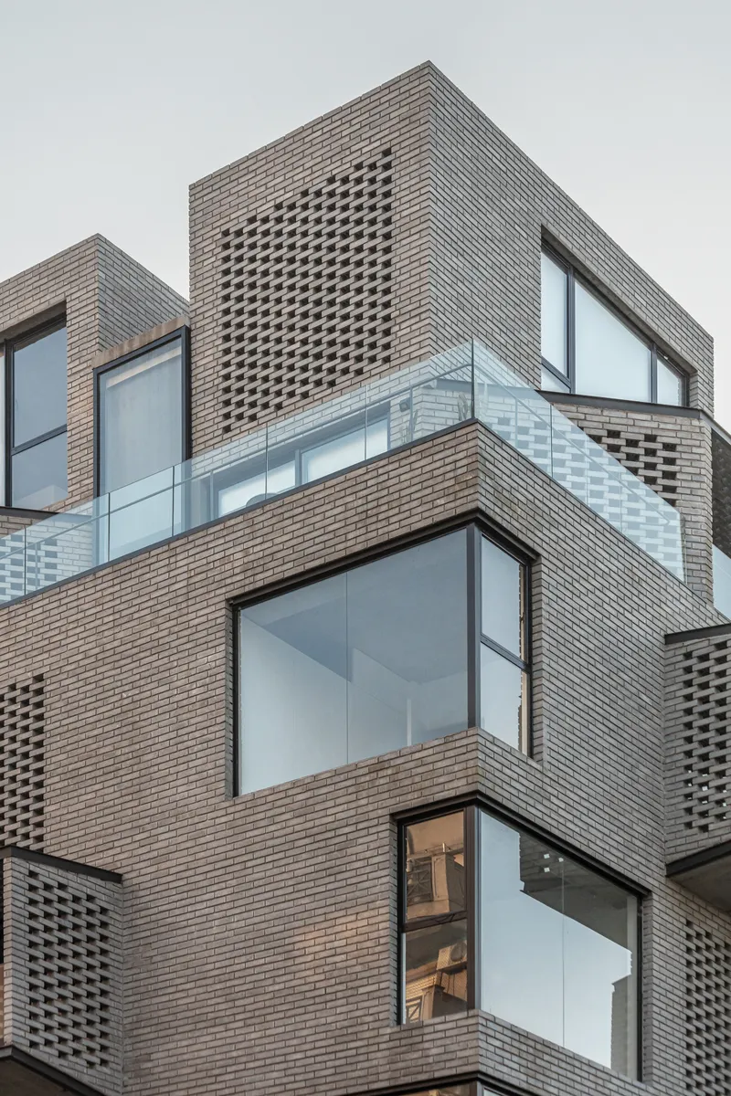 Stacked brick facade with perforated panels and large corner windows under overcast sky
