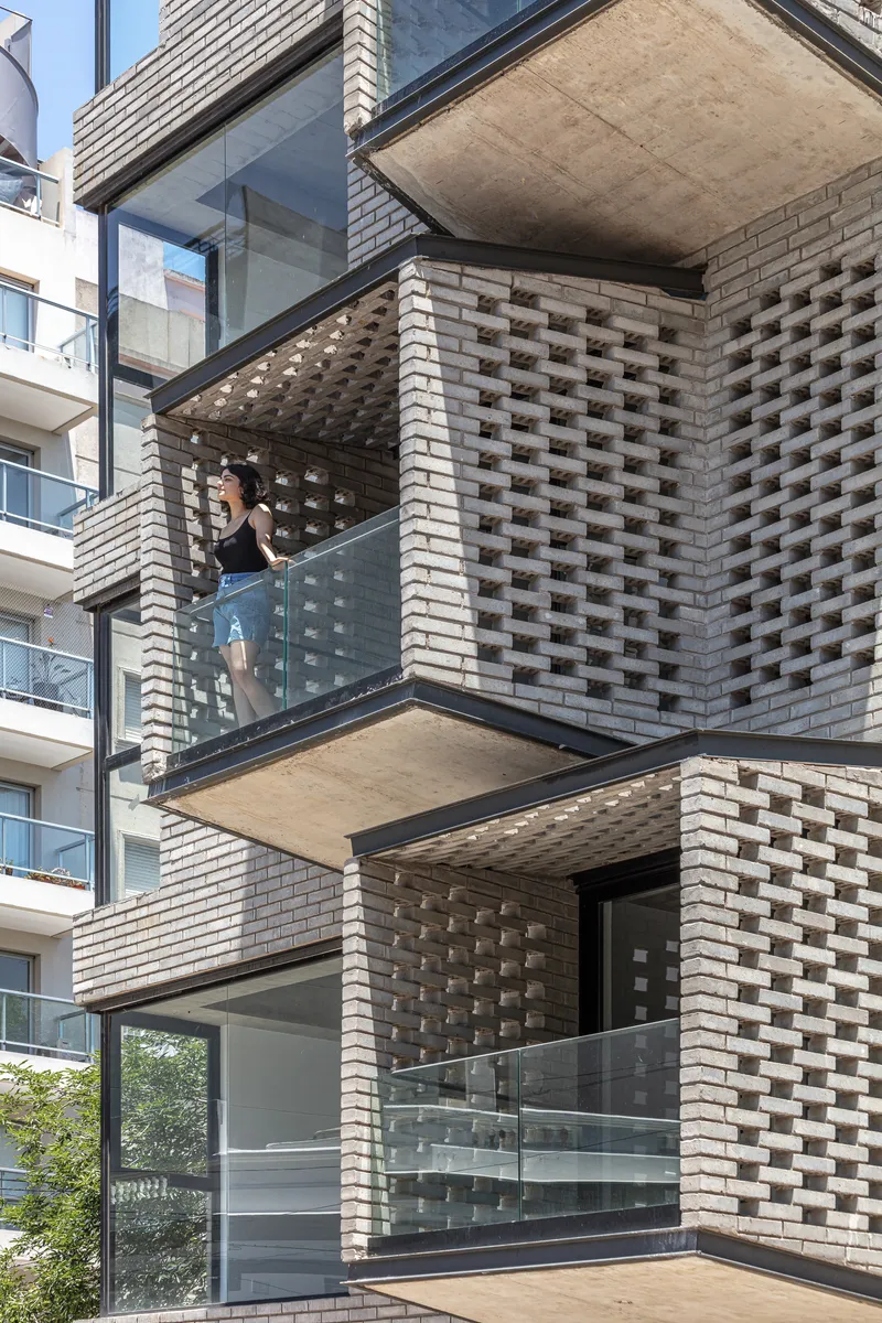 Glass-enclosed balconies with perforated brick screens and person standing inside on sunny day