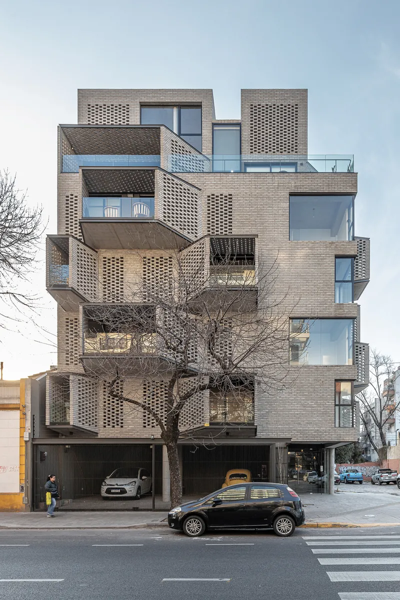 Street view of brick tower with cantilevered balconies, perforated screens, and a bare winter tree in front