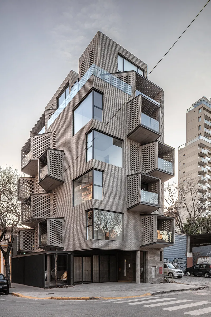 Corner elevation showing the articulated brick facade with projecting volumes and glazed openings at dusk