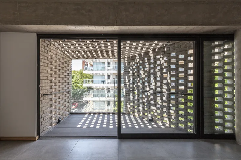 Interior view through sliding glass doors to a balcony enclosed by perforated brick screens casting dappled light