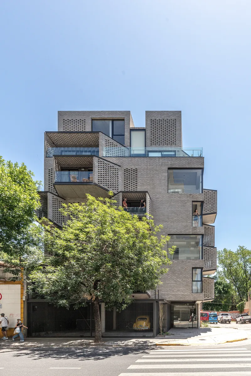 Street view of the stacked brick facade with offset balconies and perforated screens under a clear sky