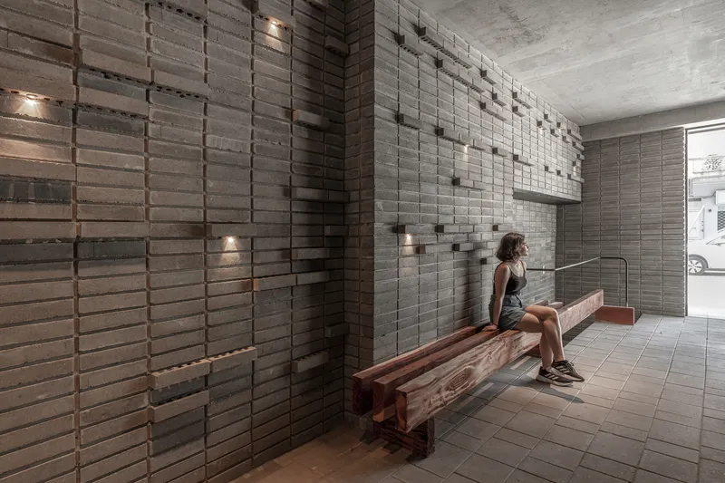 Entry vestibule with stacked brick screen walls and a person seated on a timber bench