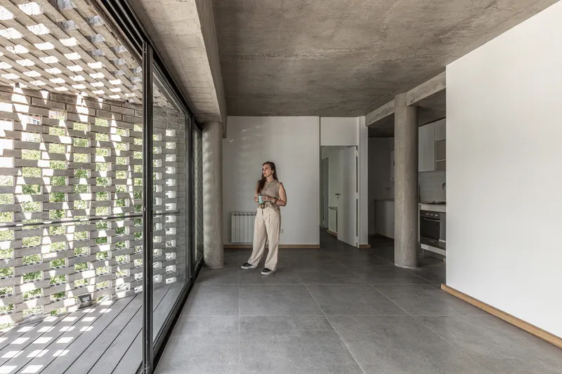 Open living space with perforated brick screen filtering daylight beside a concrete ceiling and grey tile floor