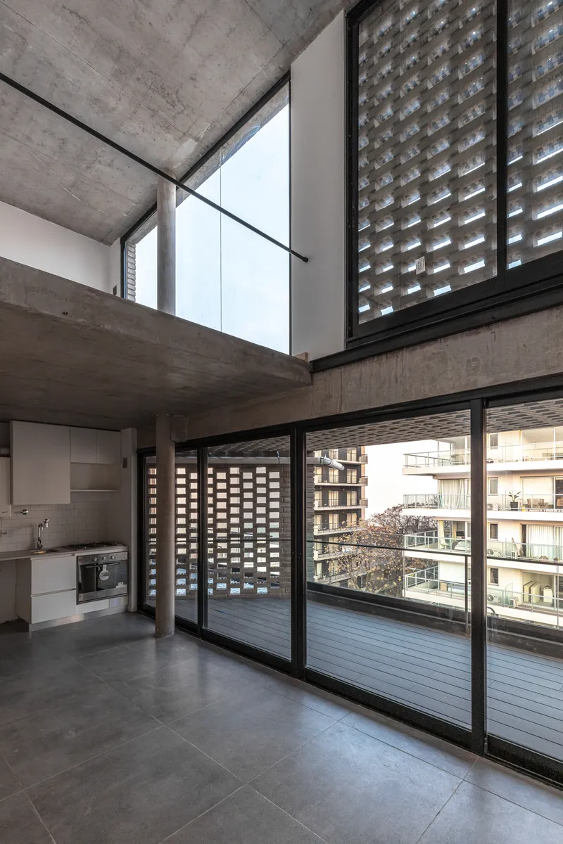 Double-height living area with mezzanine level and perforated brick screens beyond sliding glass doors