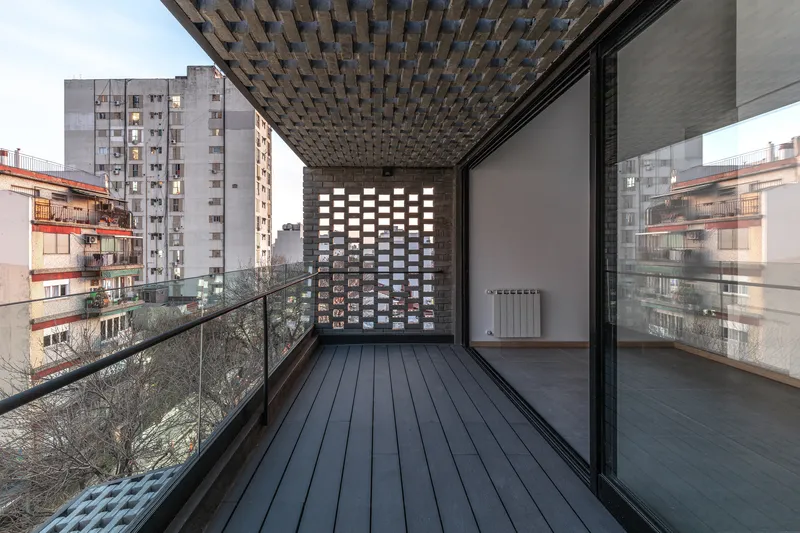 Exterior terrace with dark wood decking under a patterned brick soffit and glass railing at dusk