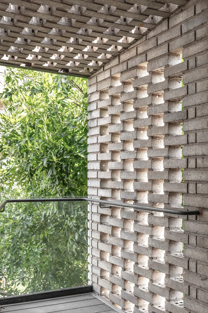 Patterned concrete block wall with open joints alongside a gridded overhead pergola and green bamboo