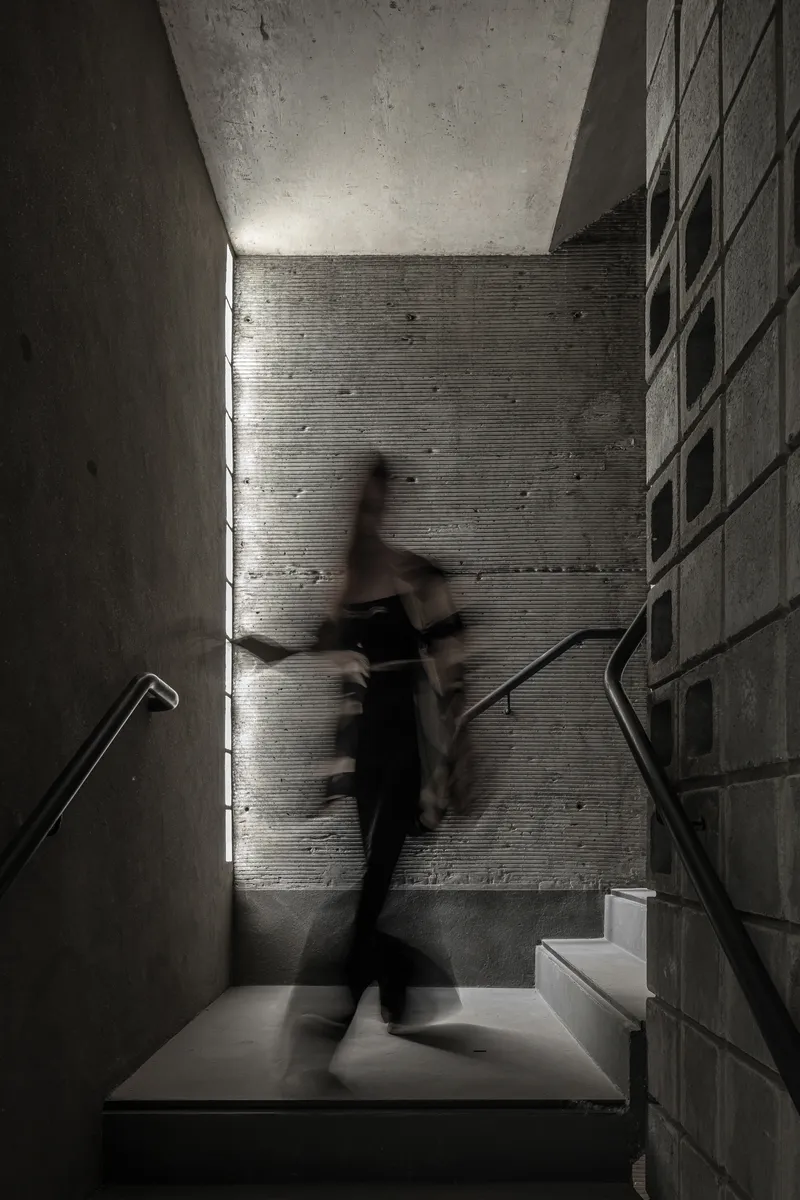 Concrete staircase landing with a figure in motion caught in daylight from a vertical slot window