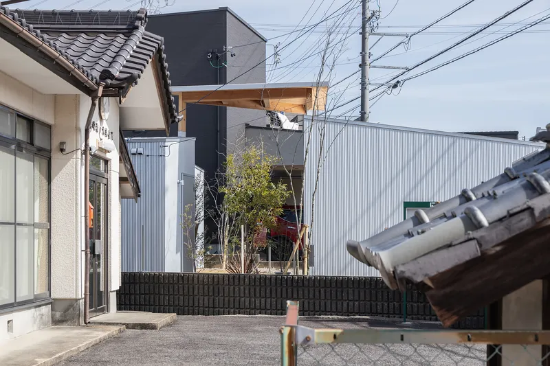 Corrugated metal facade with planted courtyard and small trees framed by traditional tiled roofs