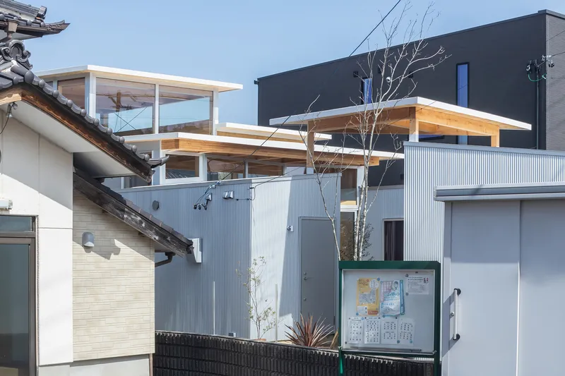Stacked volumes with flat timber roofs and glass enclosures rising above neighboring tiled roofs