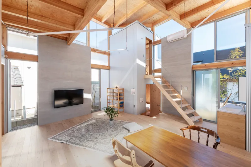 Double-height living room with exposed timber beams, an open staircase, and floor-to-ceiling windows framing the courtyard