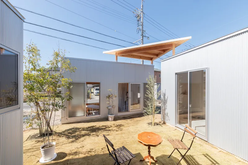 Courtyard garden with sand ground cover, planted trees, and corrugated metal-clad volumes on three sides