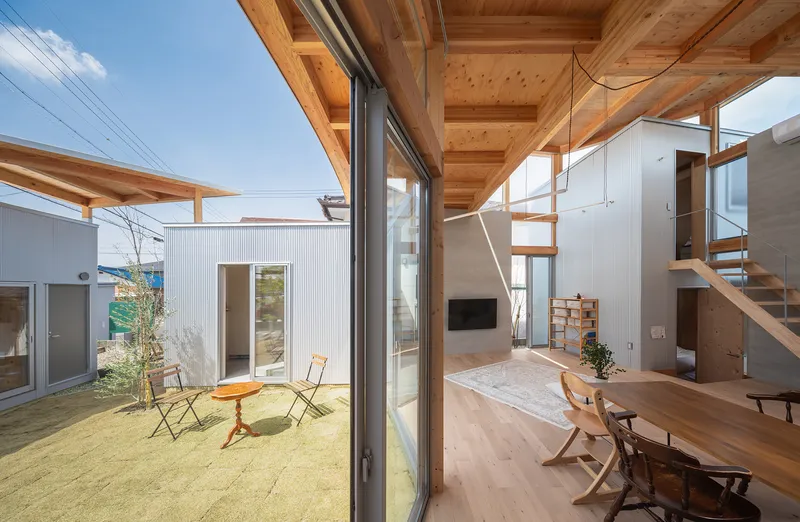 View through sliding glass doors toward a sand-filled courtyard with corrugated metal clad volumes beyond