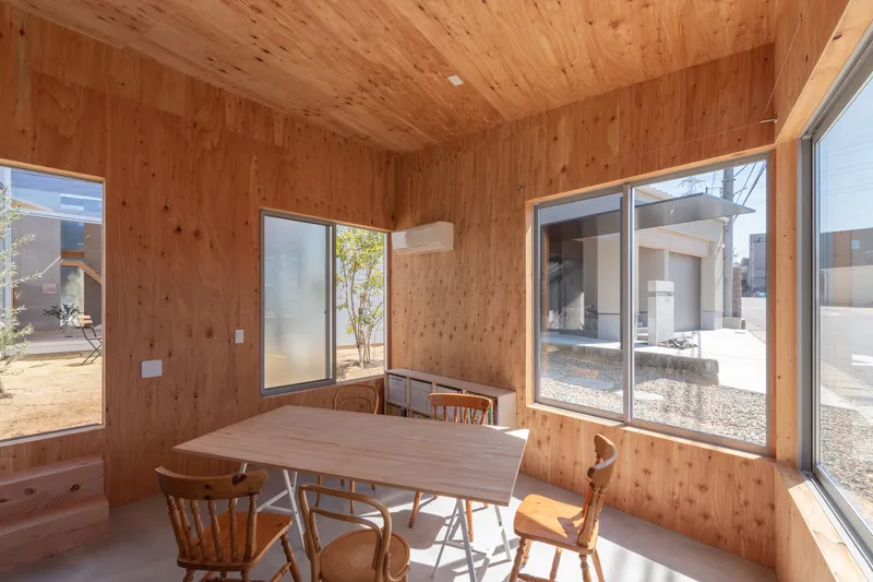 Timber-lined dining room with corner windows opening onto gravel courtyards planted with small trees