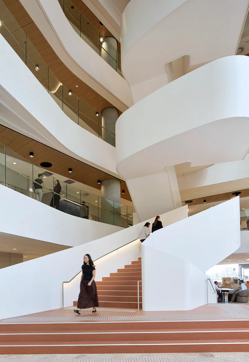 Close-up of the central staircase with person descending pink terrazzo treads between white curved walls