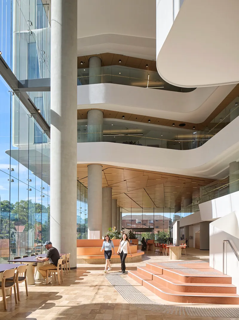 Stacked atrium balconies with curved white edges and timber soffits above terracotta-toned stepped seating