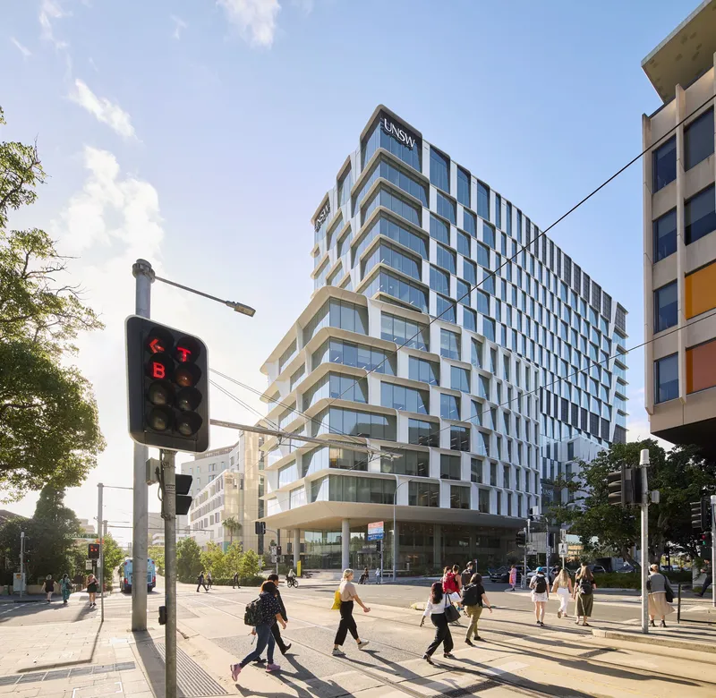 Street corner view of the stepped facade with pedestrians crossing under late afternoon light