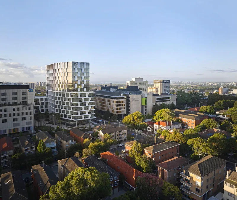 The stepped facade with offset balconies viewed from above at dusk over suburban rooftops
