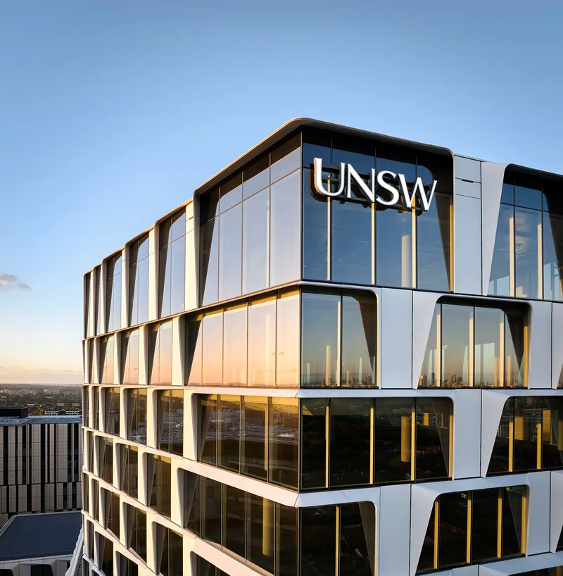 Close-up of the curved glass and metal facade with gold-toned vertical fins at sunset