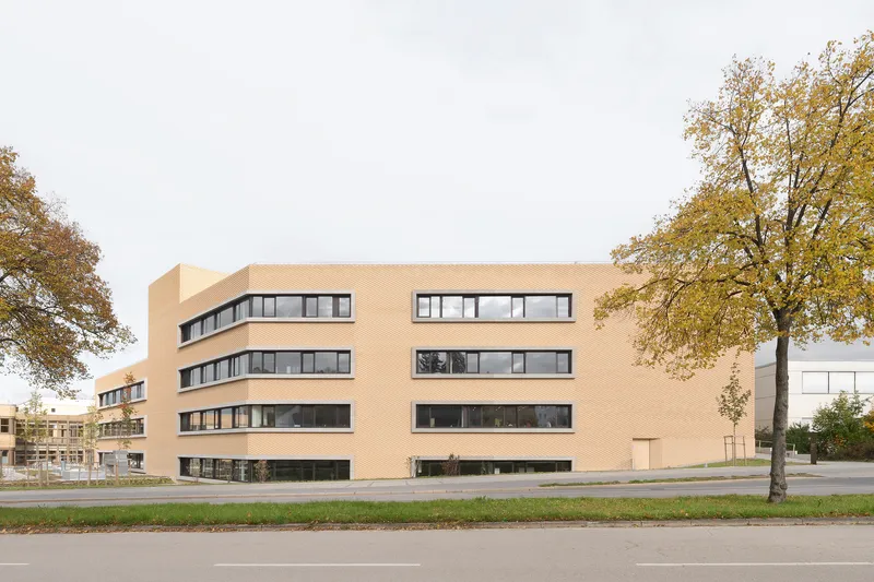 Street view of the cream brick facade with horizontal ribbon windows flanked by autumn trees