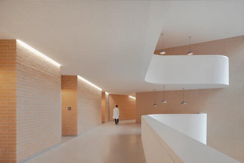 Interior corridor with yellow brick walls and linear cove lighting as a figure walks away