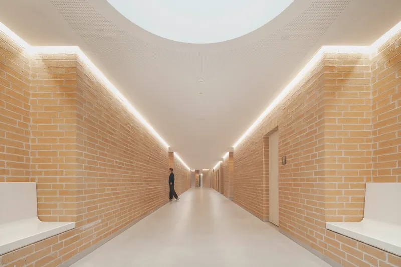 Long corridor with yellow brick walls and continuous linear cove lighting with a walking figure