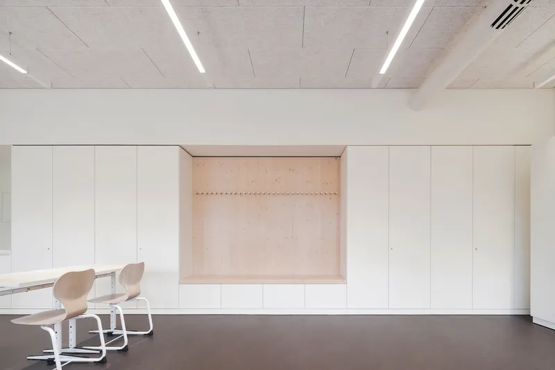 Built-in storage wall with recessed plywood niche and linear LED fixtures in the concrete ceiling