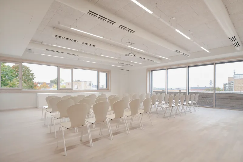 Conference space with rows of chairs facing floor-to-ceiling windows overlooking adjacent rooftops