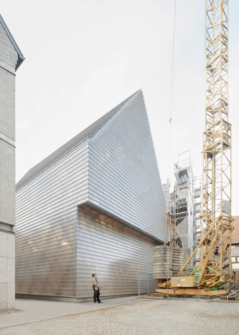 Street view showing the gabled glass brick facade beside a yellow construction crane