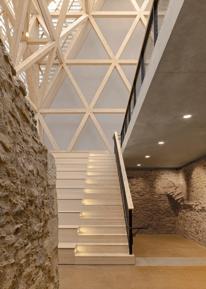 White painted staircase ascending between exposed stone wall and triangulated timber roof framework