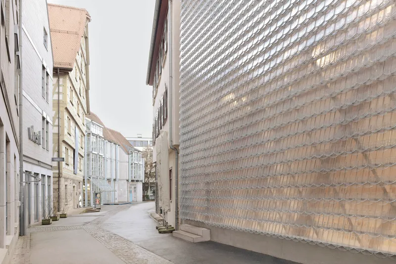 Narrow cobbled street with the textured glass brick wall rising alongside residential buildings