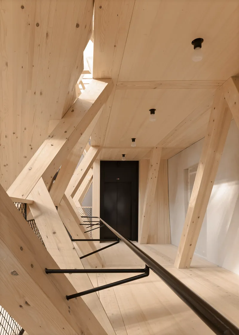 Upward view along the timber-clad stairwell with a black elevator door at the landing