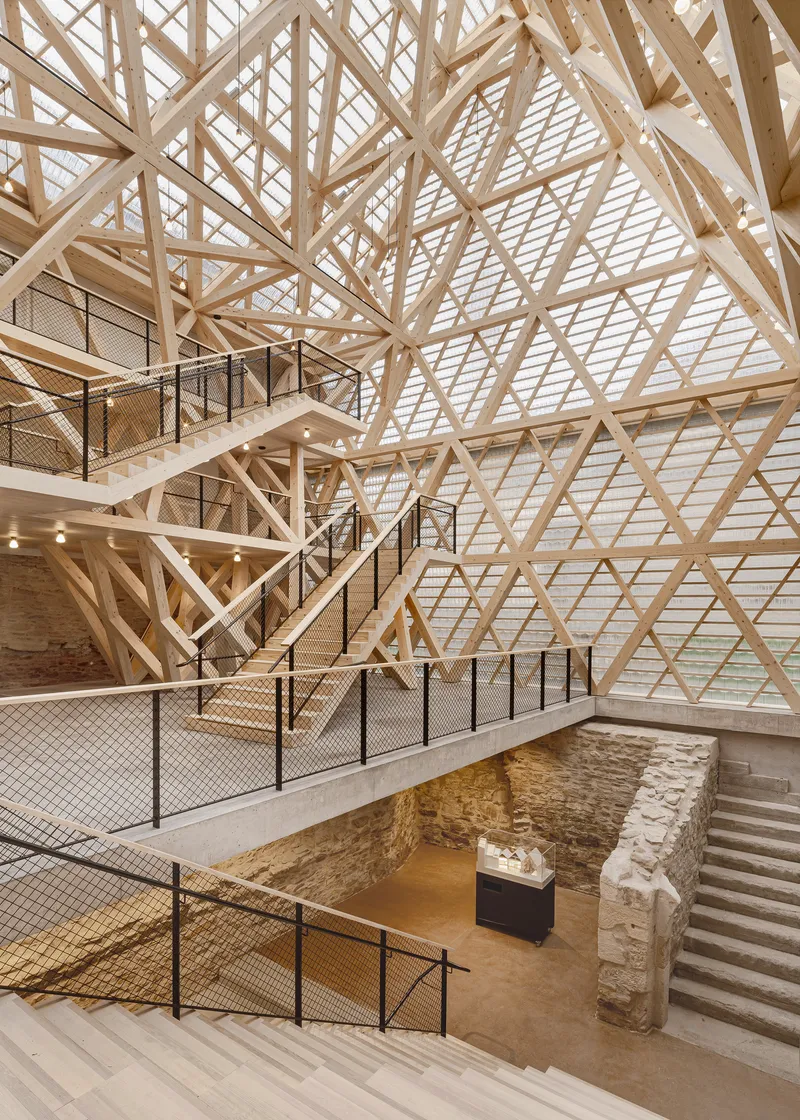 Multi-level interior showing crisscrossing staircases and exposed stone foundation walls beneath the timber lattice