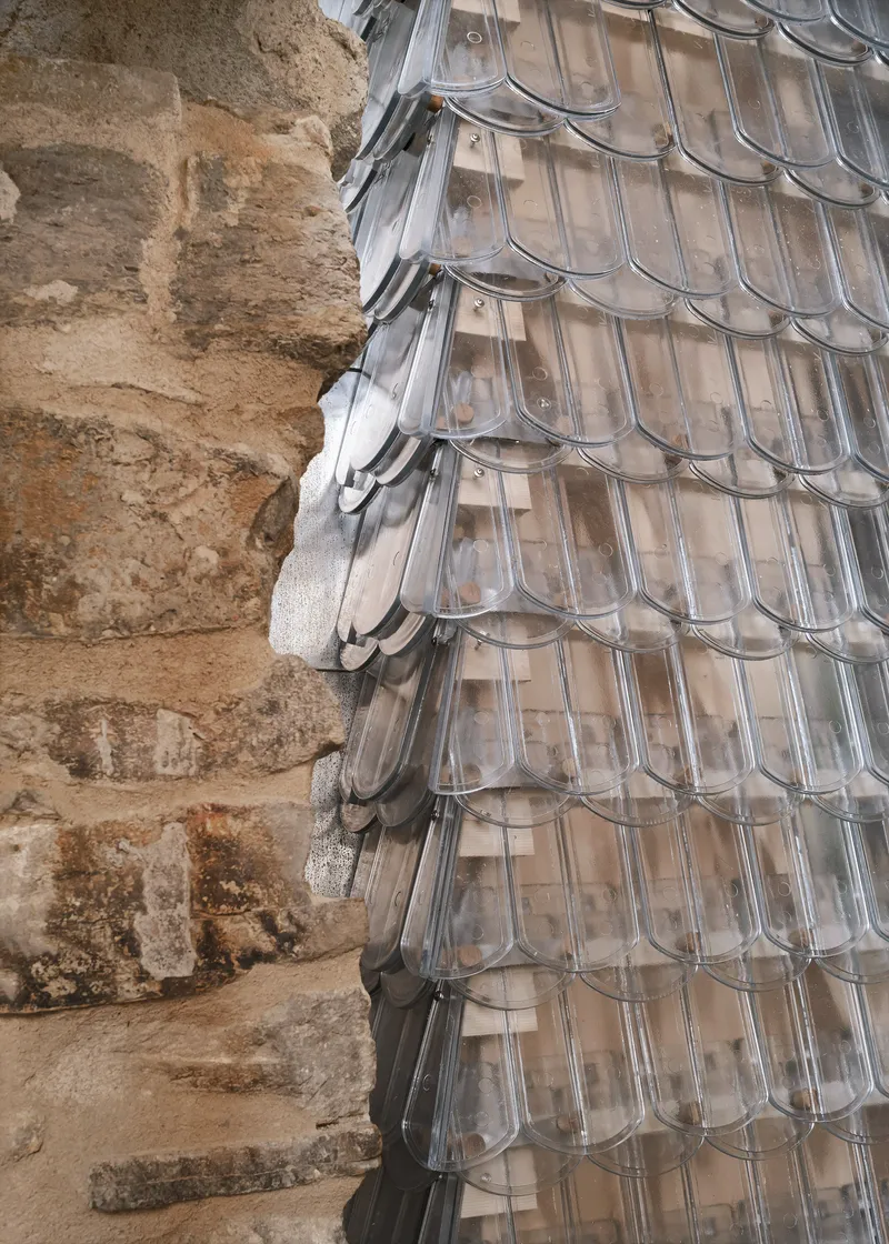 Detail of the translucent glass shingle facade meeting the excavated stone foundation wall