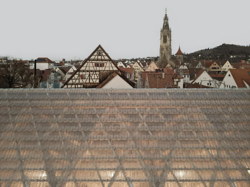 Sloped glass tile roof in the foreground with timber-framed buildings and a church spire beyond