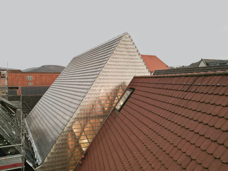 Pyramidal glass tile roof rising above surrounding red clay tile rooftops on an overcast day