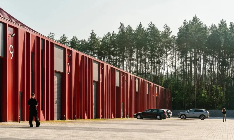 Vertical red metal fins along the warehouse facade with two parked cars and a person walking