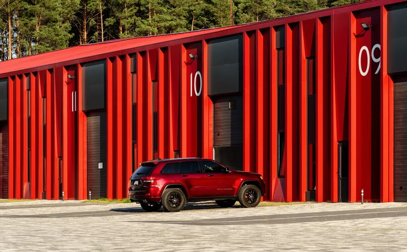 Red corrugated metal facade with numbered bays and a parked vehicle against a forest backdrop