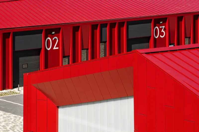 Close-up of red metal canopy projecting over white doorway with numbered units visible behind