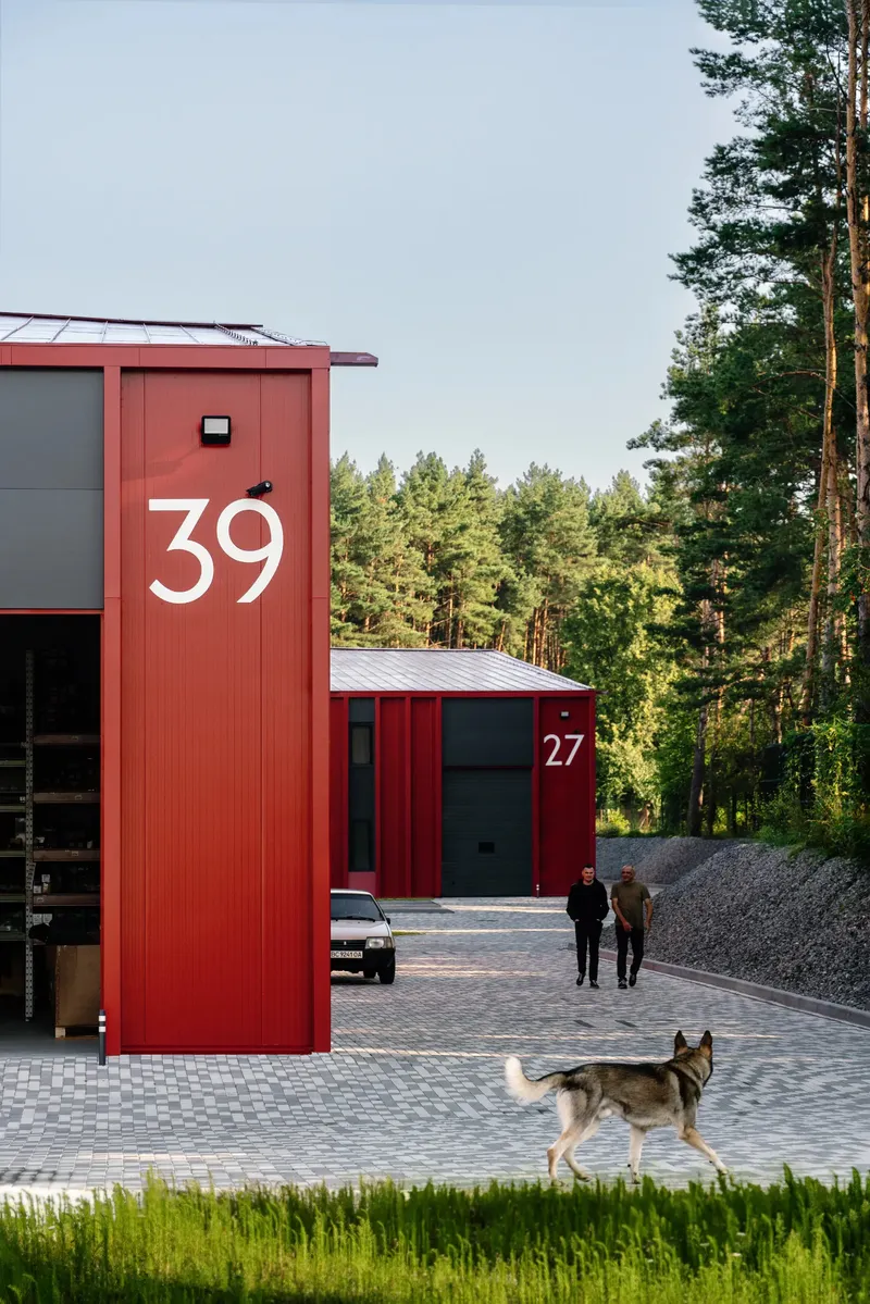 View of numbered red metal-clad units with a dog and people in a forested courtyard