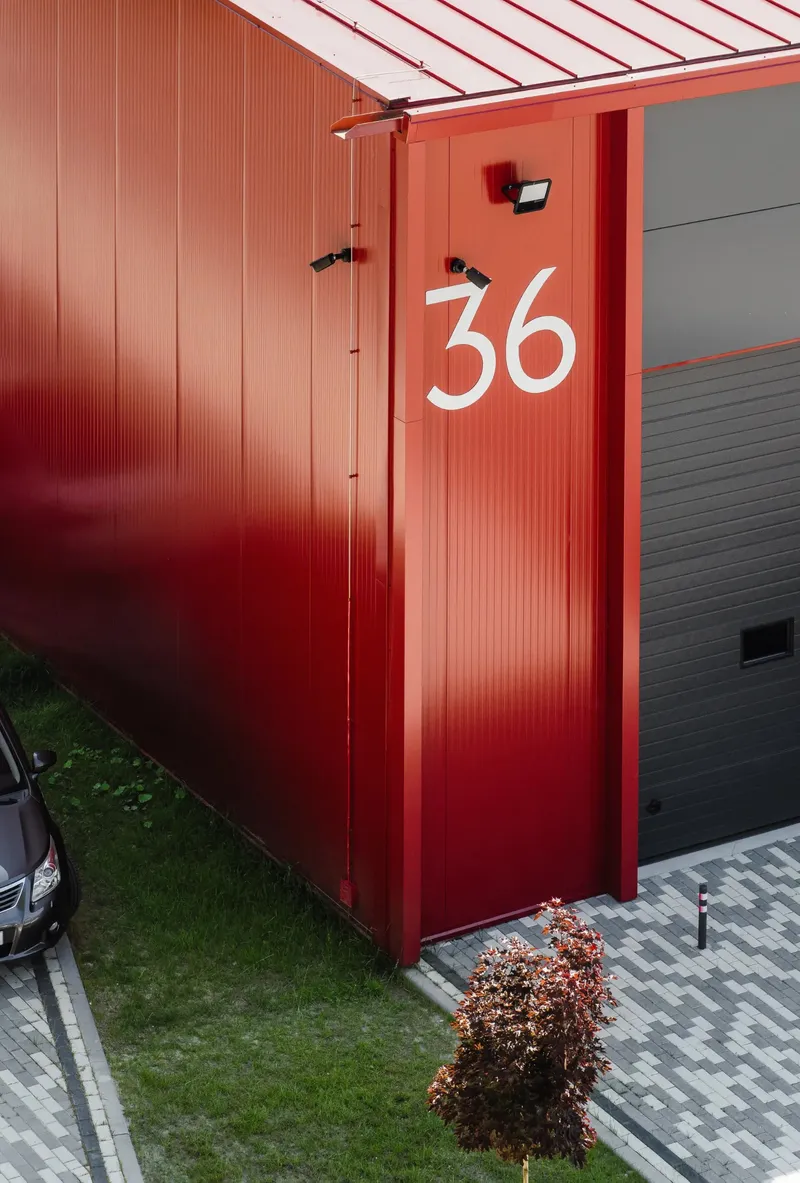 Red corrugated metal facade with white painted number 36 and a small shrub at the base