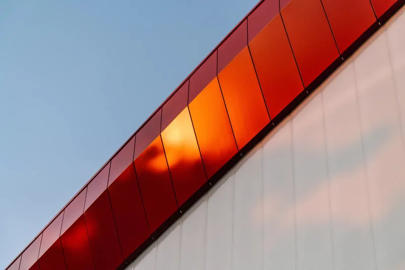 Diagonal junction between the red ribbed metal overhang and the white vertical wall panels below